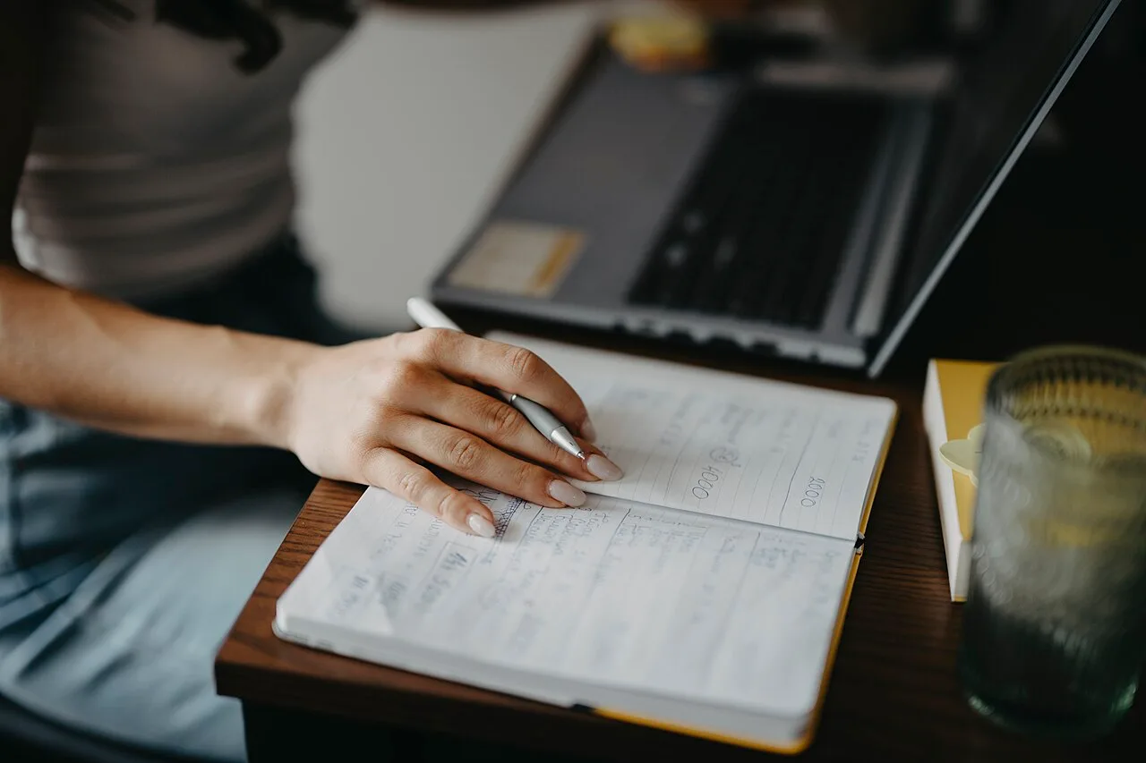 A person writing notes beside a laptop