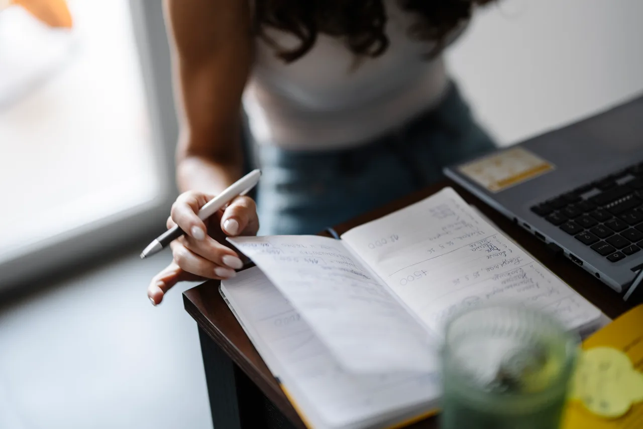 A writer using a notebook beside a laptop
